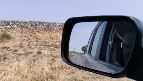 a view of barren land from a moving car and its side mirror