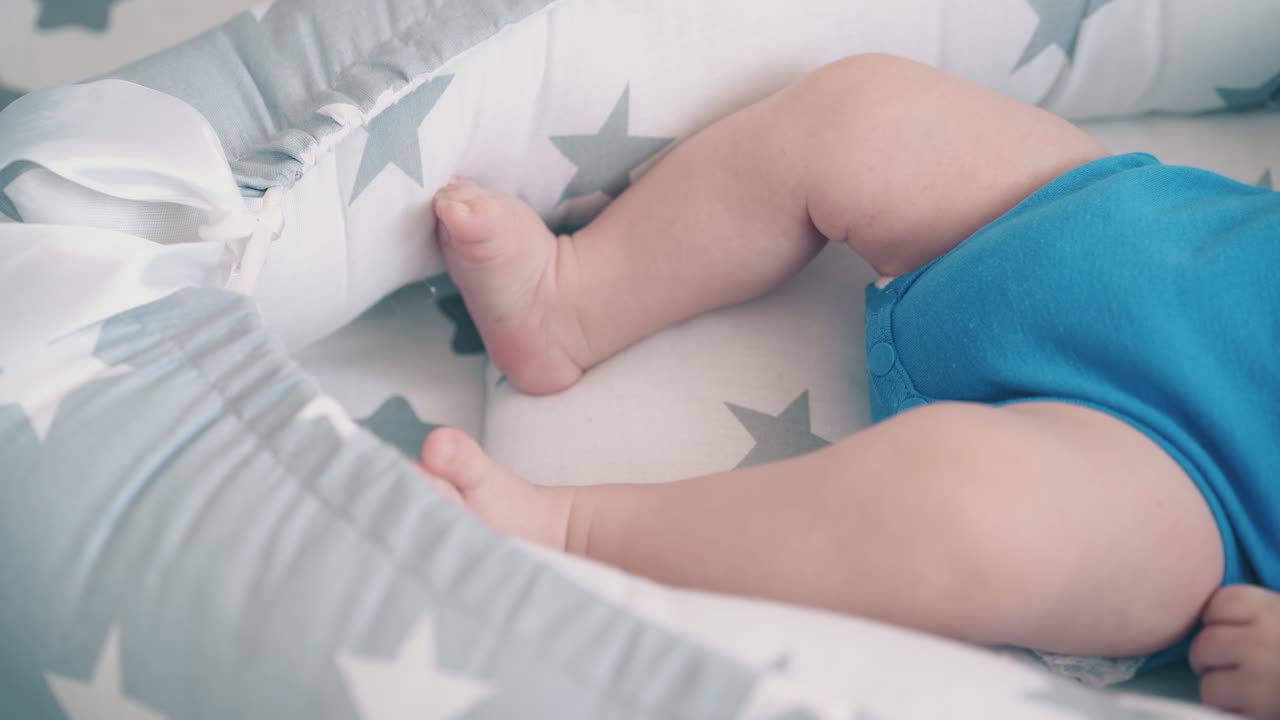 un neonato in abiti azzurri infastidisce una piccola gamba nel bozzolo