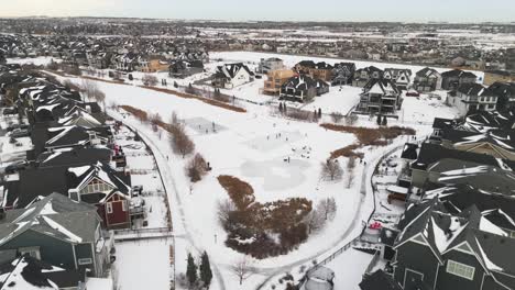 Aerial-drone-flyover-of-a-community-pond-in-Coopers-neighbourhood-in-Airdrie-Alberta-with-kids-playing-hockey