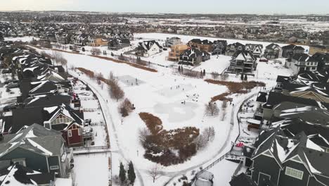 Sobrevuelo-De-Drones-Aéreos-De-Un-Estanque-Comunitario-En-El-Barrio-De-Coopers-En-Airdrie-Alberta-Con-Niños-Jugando-Al-Hockey