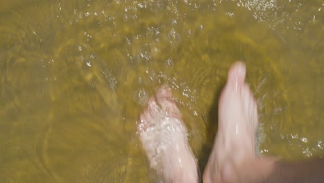 top view of male feet walking on beach sand in low sea water, sunny day