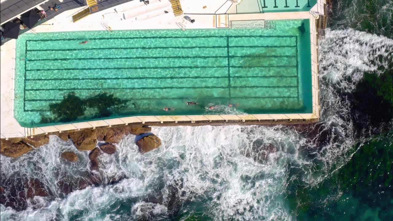 Fugleperspektiv over Bondi Icebergs Pool med bølger, der slår mod klipperne ved Bondi Icebergs Club, New South Wales, Australien.
