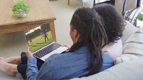 pareja biracial portátil con diversos jugadores de fútbol masculino jugando partido en la pantalla