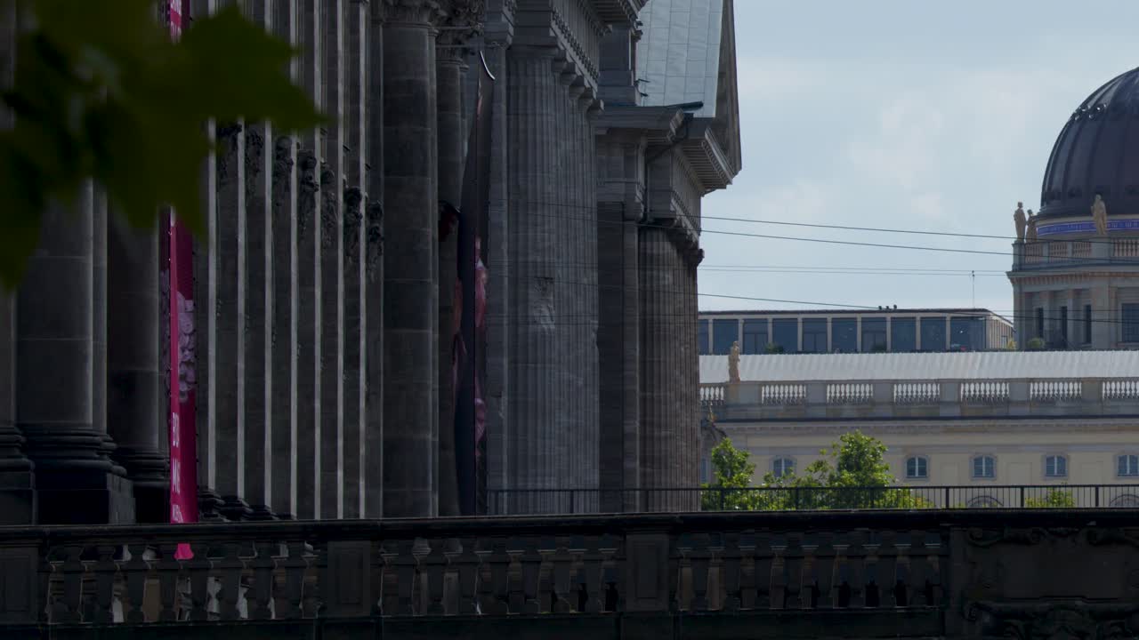 Camera slowly pans right, unveiling classical columns and domed building under daylight sky