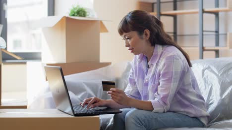 Mujer-Con-Computadora-Portátil-Y-Tarjeta-De-Crédito-En-Casa-Nueva.-Mudanza,-Personas-Y-Concepto-De-Bienes-Raíces.-Mujer-Asiática-Feliz-Y-Sonriente-Con-Computadora-Portátil-Y-Tarjeta-De-Crédito-En-Casa-Nueva.