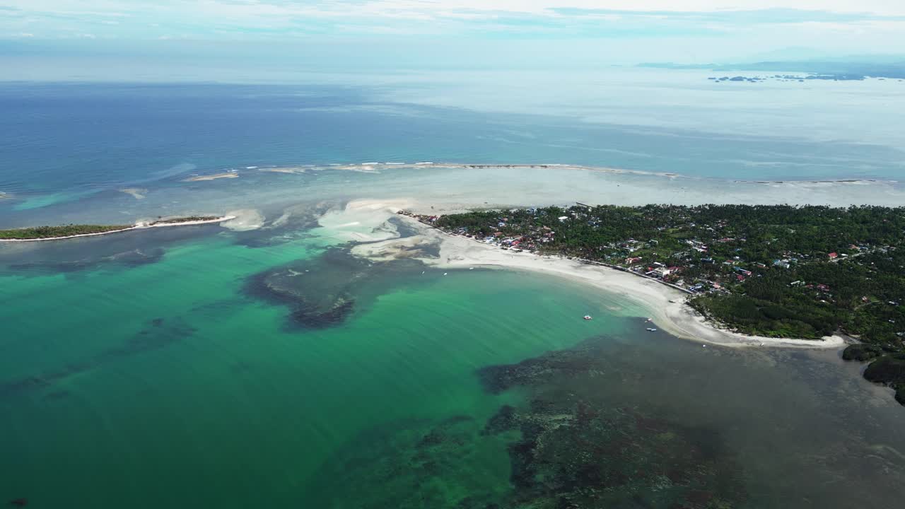 Komposisi aerial terpusat yang menangkap garis pantai pulau, pohon palem, pasir putih, dan air dangkal di Tondol