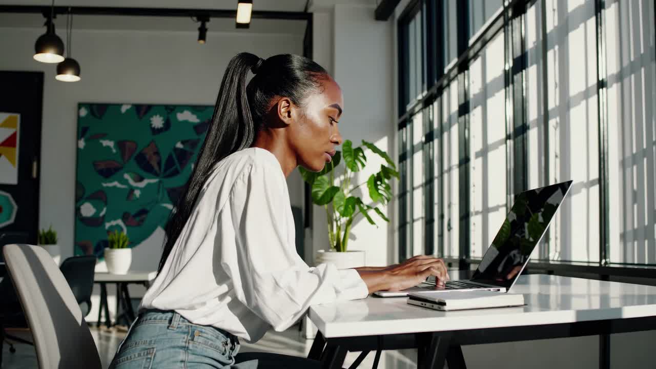 Side angle of a woman working on a laptop in a modern office
