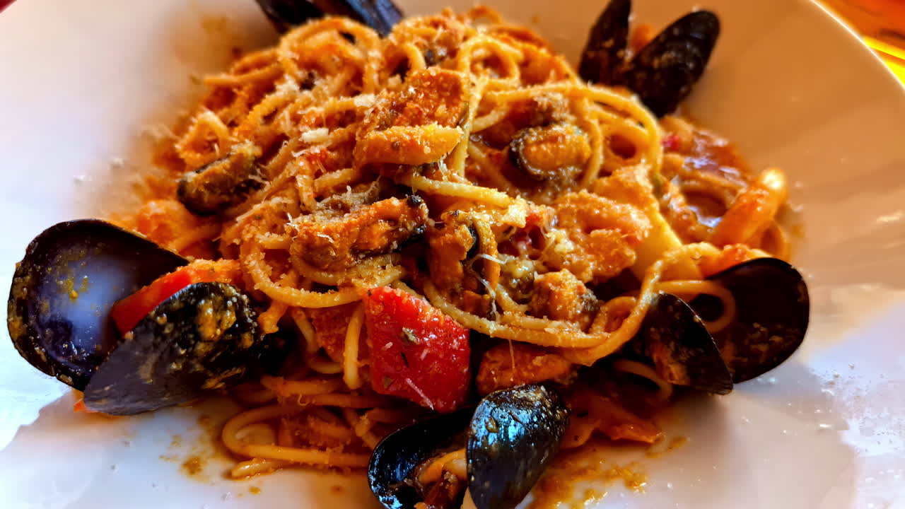 Red seafood pasta with mussels in the shell sprinkled with parmesan cheese - close up pullback reveal