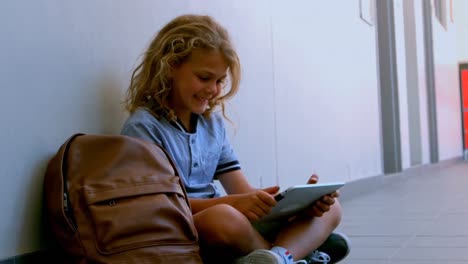 linda colegiala caucásica sentada en el suelo y usando una tableta digital en el pasillo de la escuela 4k
