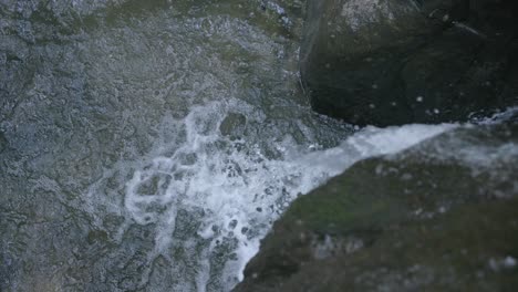 imágenes en cámara lenta de agua estrellándose contra una roca y cayendo en un charco de agua