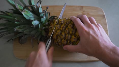 man places pineapple on cutting board and begins to prepare the delicious fruit