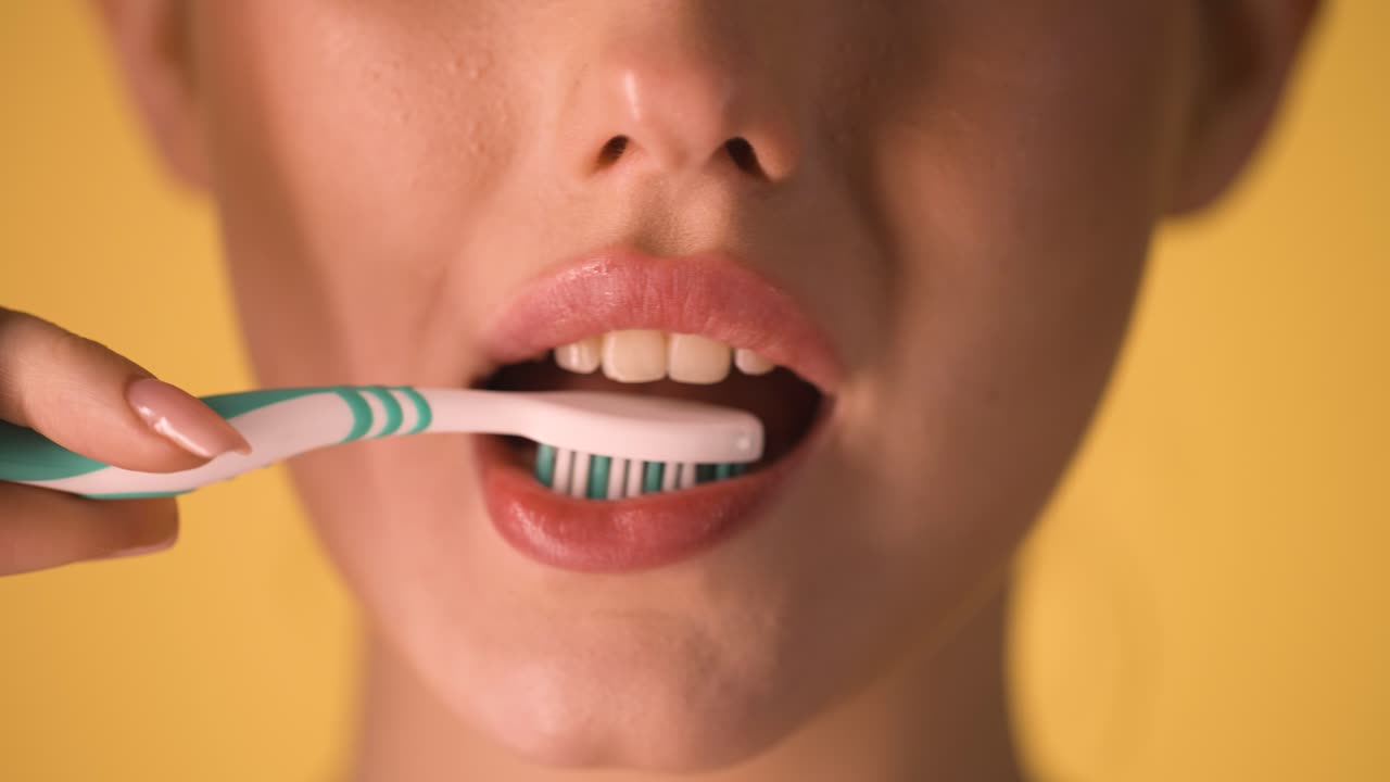 joven mujer caucásica se cepilla los dientes con cepillo de dientes, primer plano de la cara, toma de fondo cromático, higiene oral