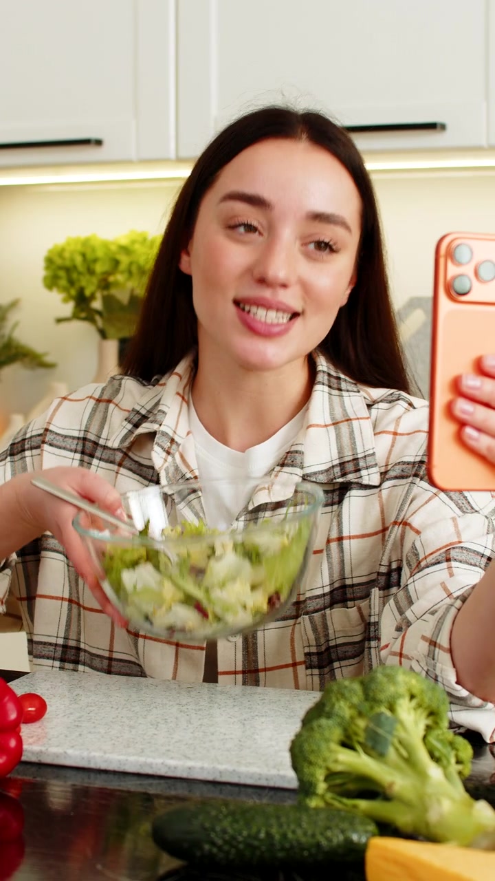 Joven vloguera graba consejos de cocina keto saludable presentando una ensalada de verduras a sus seguidores por teléfono