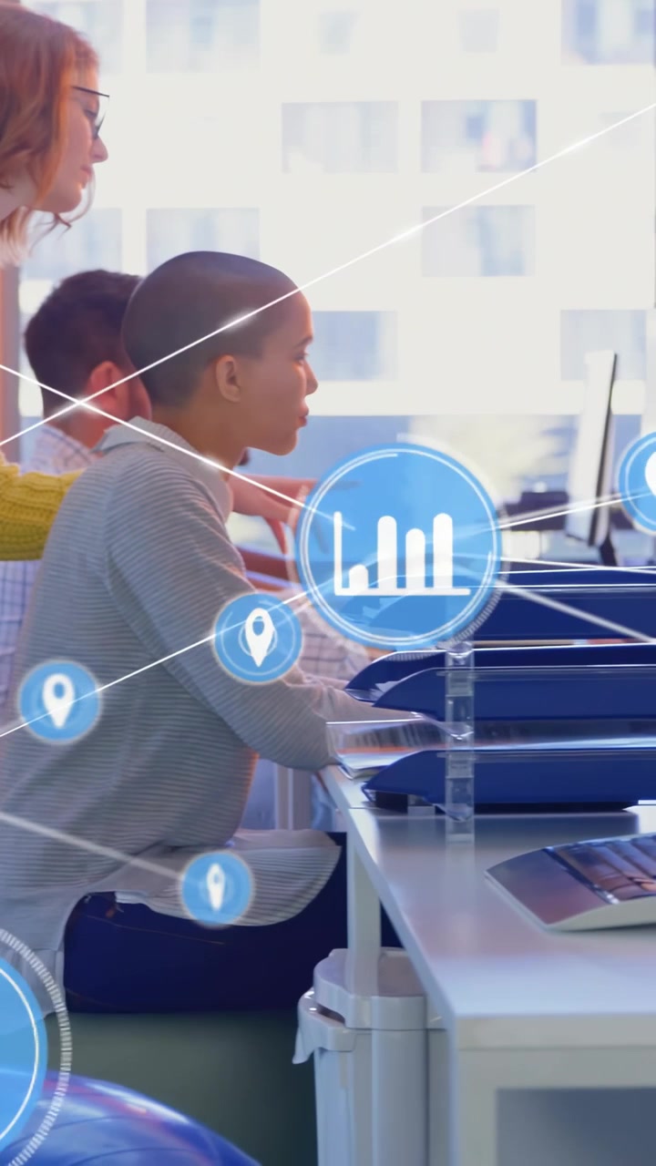 Vertical video: Seated analyst typing, peer leaning and pointing, driving data map growth for tech