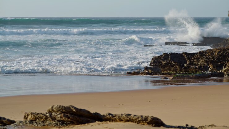 L'océan déferle sur une plage rocheuse par une journée ensoleillée. Des vagues blanches et écumeuses s'étirent le long du littoral.