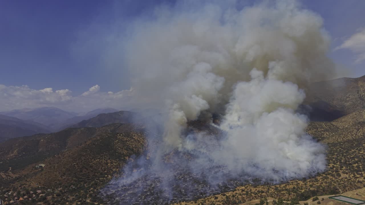 Vista aerea cinematografica ad alta quota realizzata con drone di un enorme incendio che produce un imponente pennacchio di fumo sulle Ande, Cile, 4K