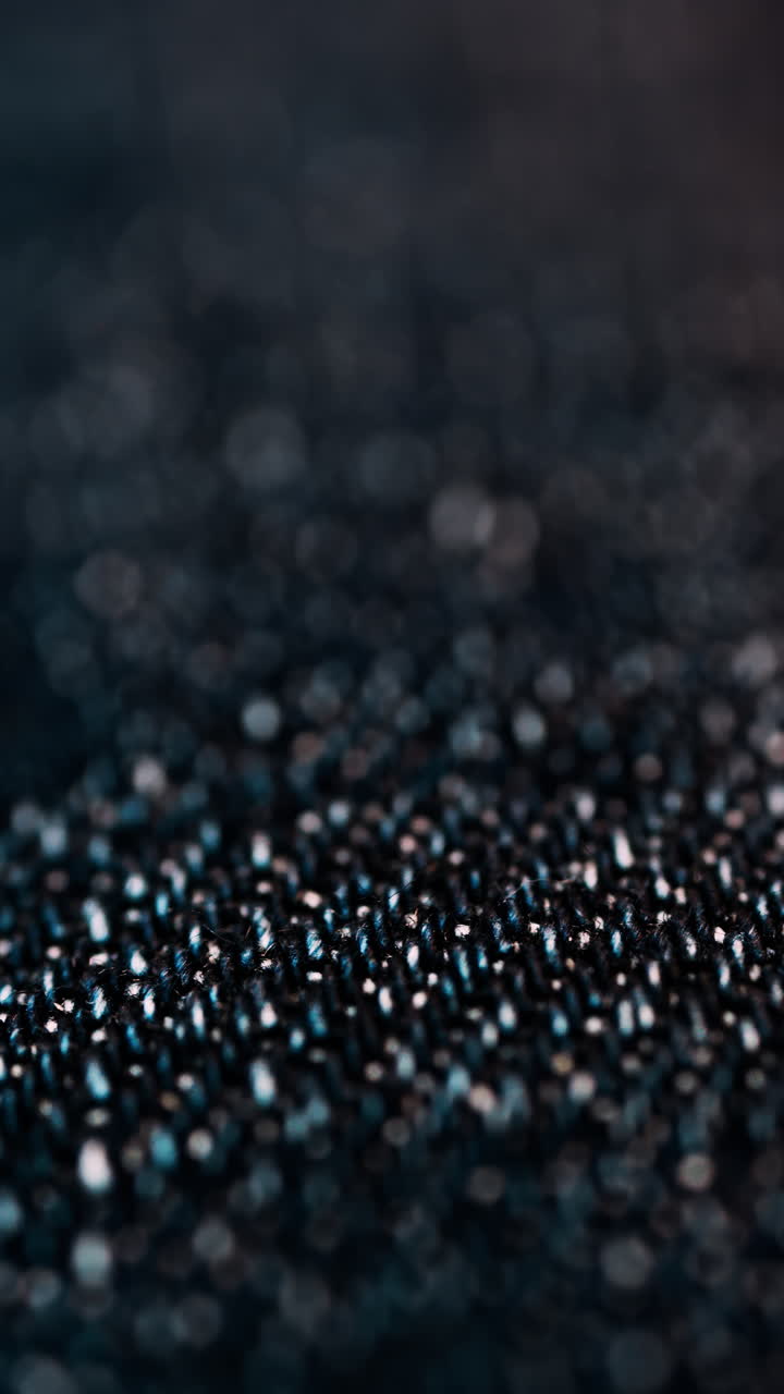 Primo piano di un tessuto denim scuro, con piccole fibre riflettenti. Verticale