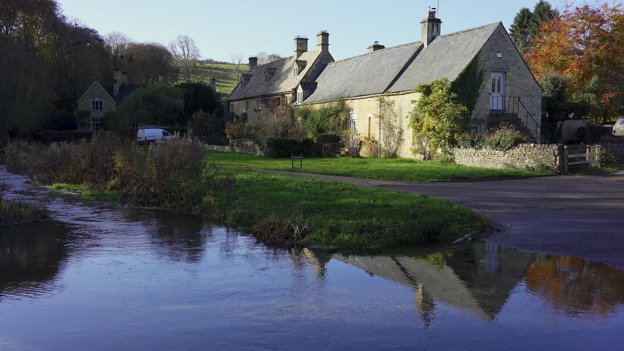Maleriske hytter spejler sig i et vadested, der krydser en lavvandet flod i Upper Slaughter, en historisk landsby i den berømte Cotswolds-region