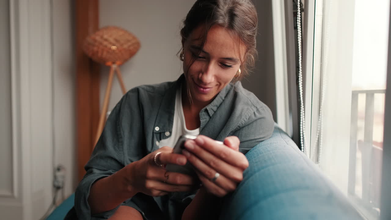 Happy Young Woman Sitting on Couch and Using Smartphone