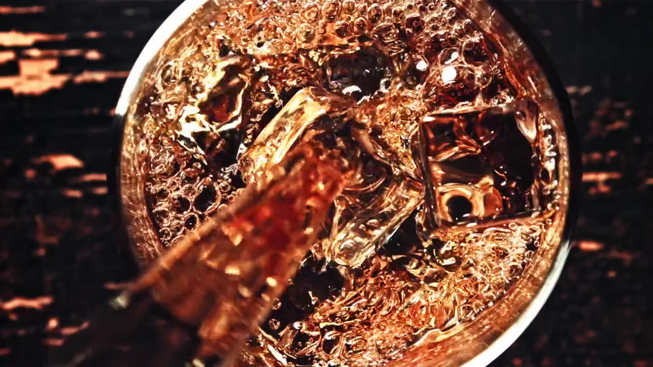 Versamento al rallentatore di cola rinfrescante in un bicchiere con ghiaccio