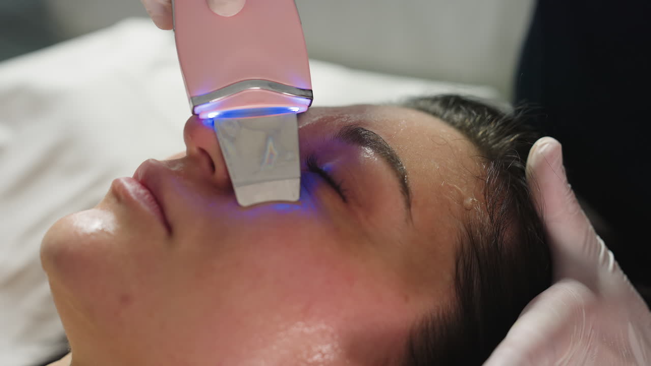 Beauty specialist wearing gloves glides ultrasonic wand over client face to gently extract pimples and impurities during advanced skin treatment session in luxury modern spa environment