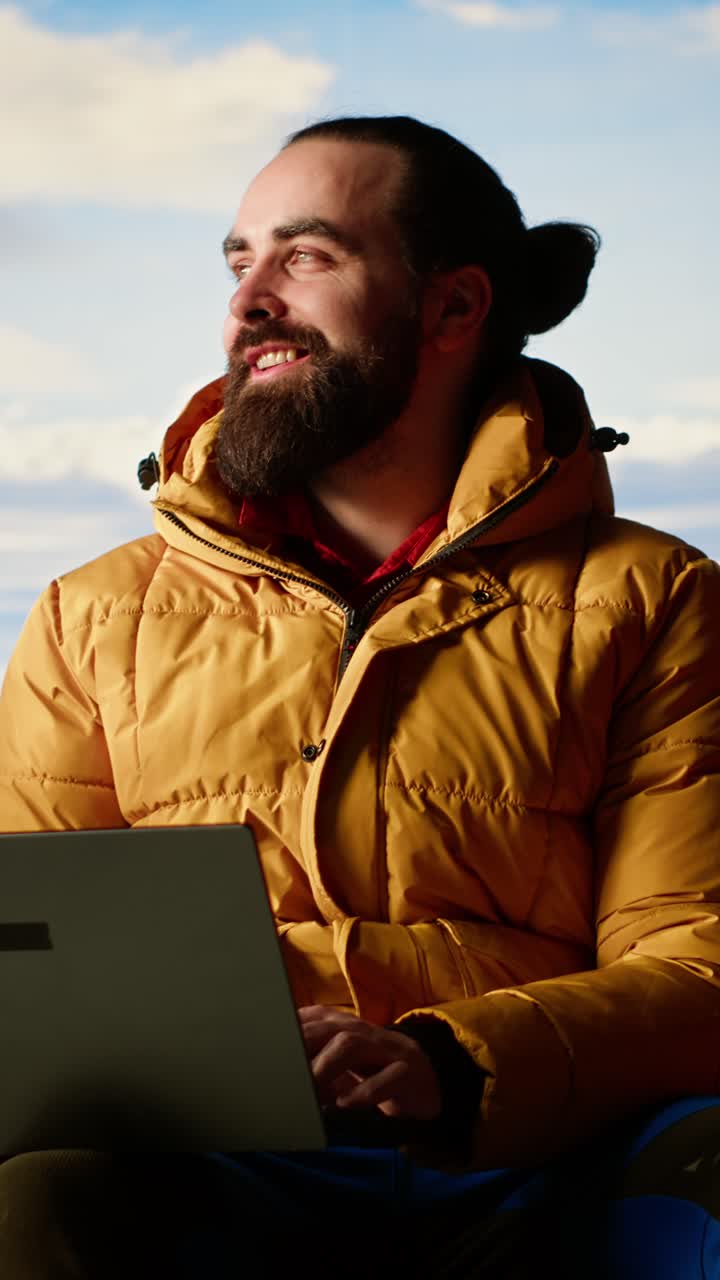 Uomo barbuto che lavora al computer portatile all'aperto con sfondo di cielo blu