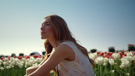 thoughtful girl sitting in flower field in sunlight. woman dreaming among tulips