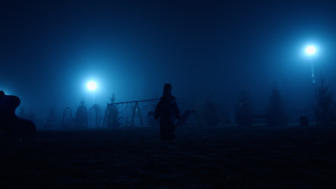 Toddler kid's silhouette heading to the playground outdoors at night. Baby wearing warm clothes in the park.
