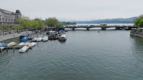 Disparo-De-Drones-En-Movimiento-Hacia-Adelante-Siguiendo-El-Río-Hacia-El-Puente-Principal-Que-Conduce-Al-Lago-Zurich