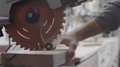 hands of carpenter cutting off thin piece of wood from blank on miter saw