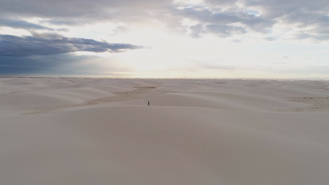 vista aérea de una persona caminando en un vasto campo de dunas de arena blanca al amanecer, 4k