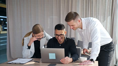 co-working young office team looking at computer screen. employees smiling and discussing something on laptop.