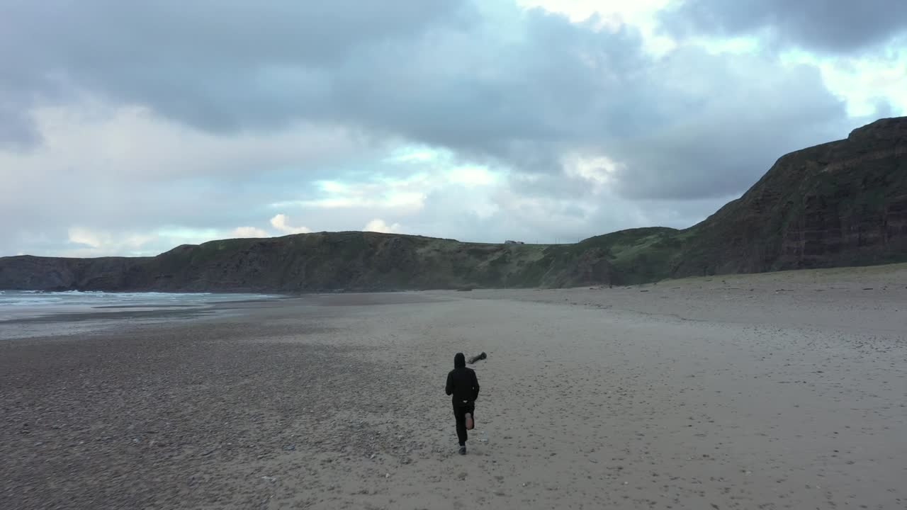 백미러 공중 추적, 절벽으로 둘러싸인 모래 해변에서 달리는 남자