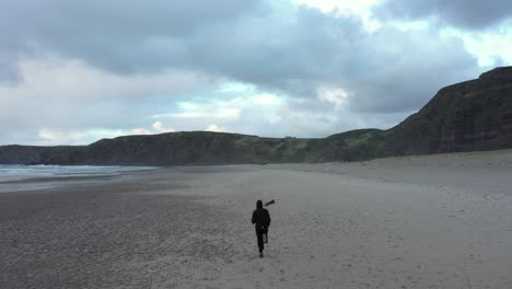 seguimiento de la antena retrovisora, hombre corriendo en la playa de arena rodeada de acantilados