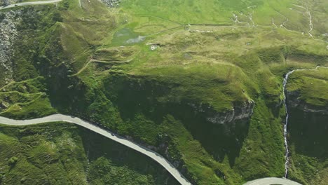 an aerial video shows a serpentine mountain road snaking through a lush, green landscape. multiple switchbacks and vehicles are visible, emphasizing the road's dramatic curves and elevation.