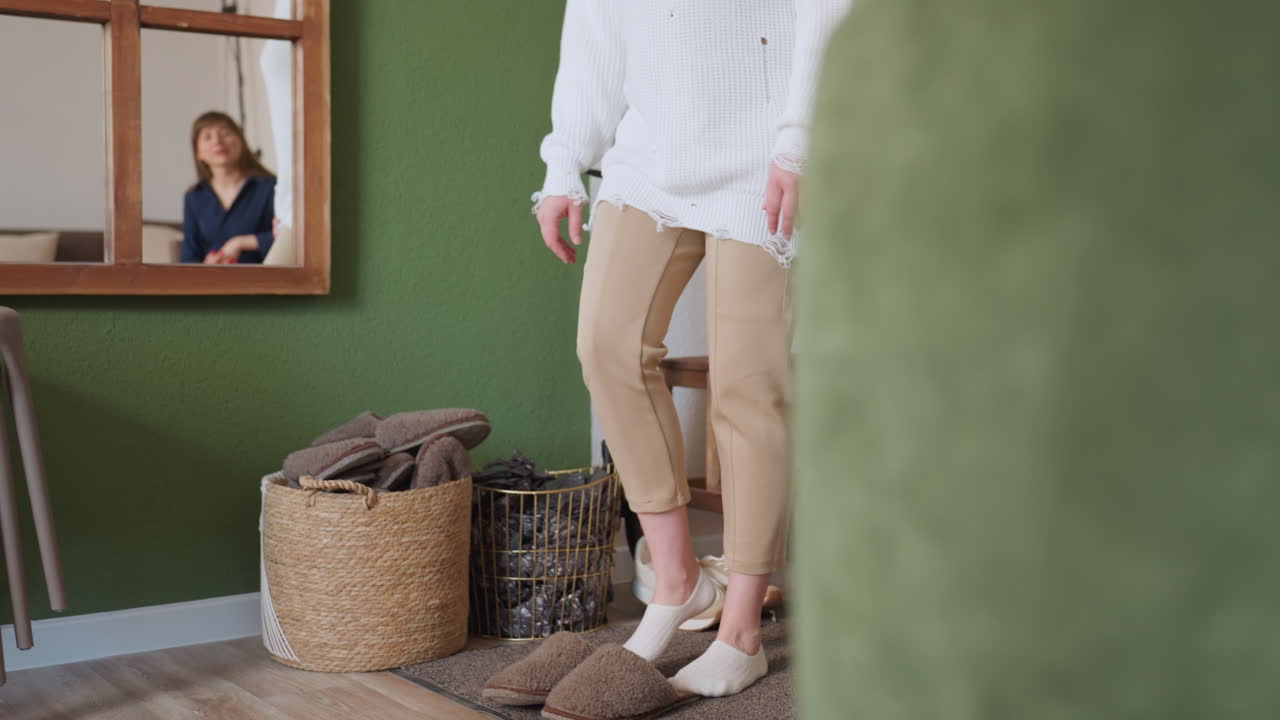 Client walks toward door wearing socks after removing shoes, therapist sits calmly on sofa waiting, mirror reflects interaction in softly lit interior with coat rack, and cozy therapeutic setting