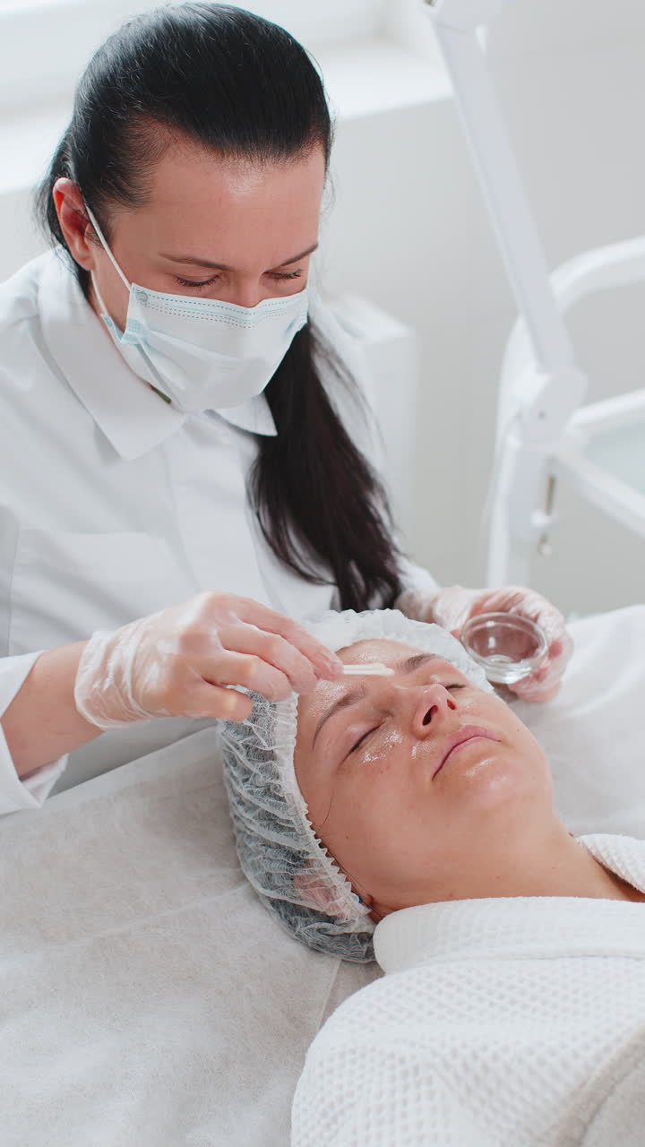 Cosmetologist applying special moisturizing acid serum peeling face of caucasian woman in clinic