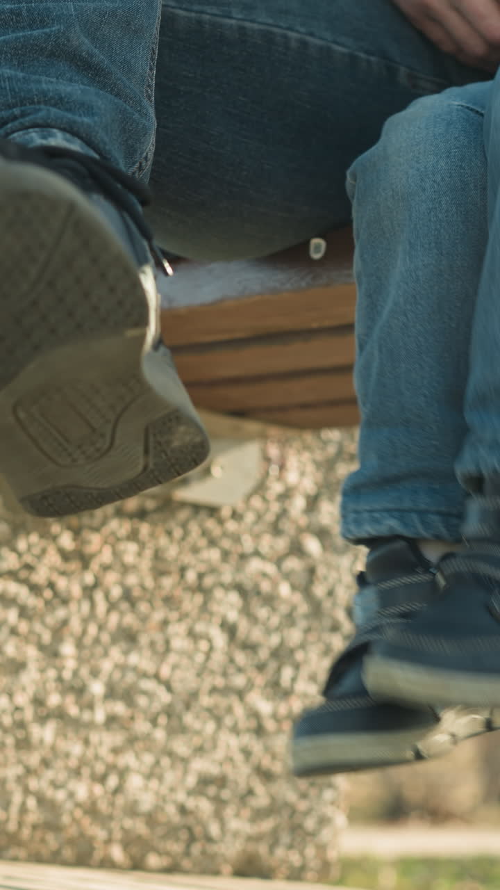 벤치에 가까이 앉아있는 어른과 아이의 클로즈업, 아이가 놀이로 다리를 흔들고 어른이 십자 다리를 움직이고, 나무의 흐릿한 배경