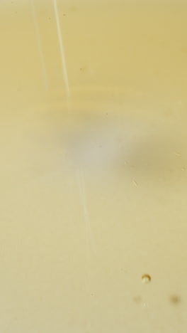Drops of jojoba oil fall on white surface leaving round traces. Golden oily liquid with small bubbles slowly spreading on table extreme closeup