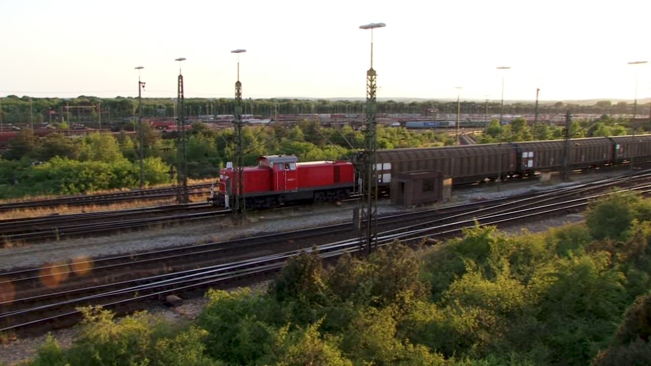 Red train moving through lush green railway at sunset, peaceful scene