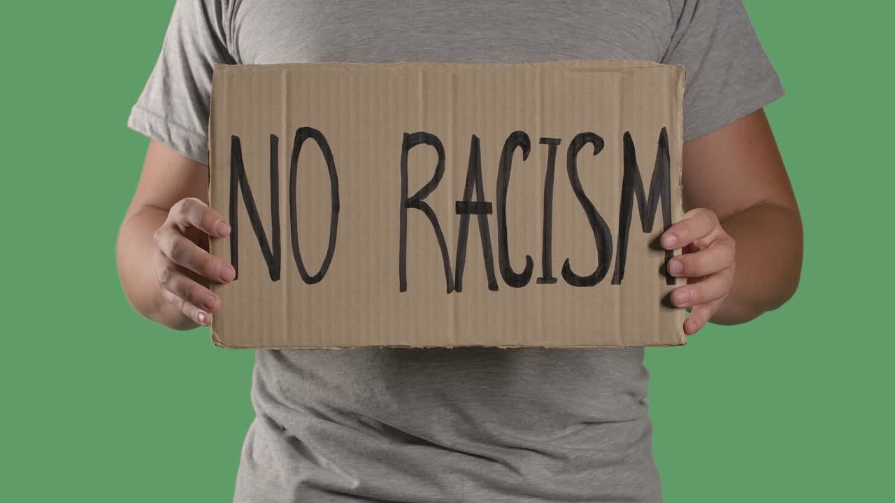 Man holds in front of him a poster from a cardboard box with the words NO RACISM. Concept of strike and anti racism. Isolated a green screen, chroma key. Close up. Slow motion