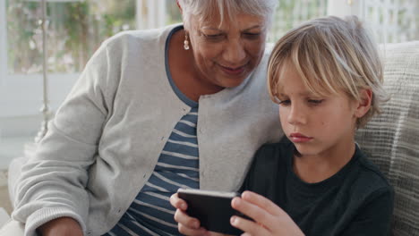 Niño-Feliz-Usando-Un-Teléfono-Inteligente-Mostrando-A-La-Abuela-Cómo-Usar-El-Teléfono-Móvil-Enseñando-A-La-Abuela-Tecnología-Moderna-Niño-Inteligente-Ayudando-A-La-Abuela-En-Casa-4k