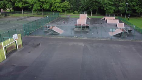 Vista-Aérea-Volando-Por-Encima-De-La-Cancha-De-Baloncesto-Cercada-Y-La-Rampa-Del-Parque-De-Patinaje-En-Un-Patio-Vacío-Y-Cerrado