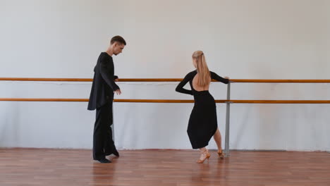 two dancers practicing in a studio with a ballet barre