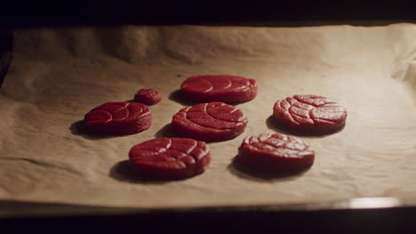una persona pone a mano una bandeja para hornear dentro del horno con masa de galleta roja cruda, cierra