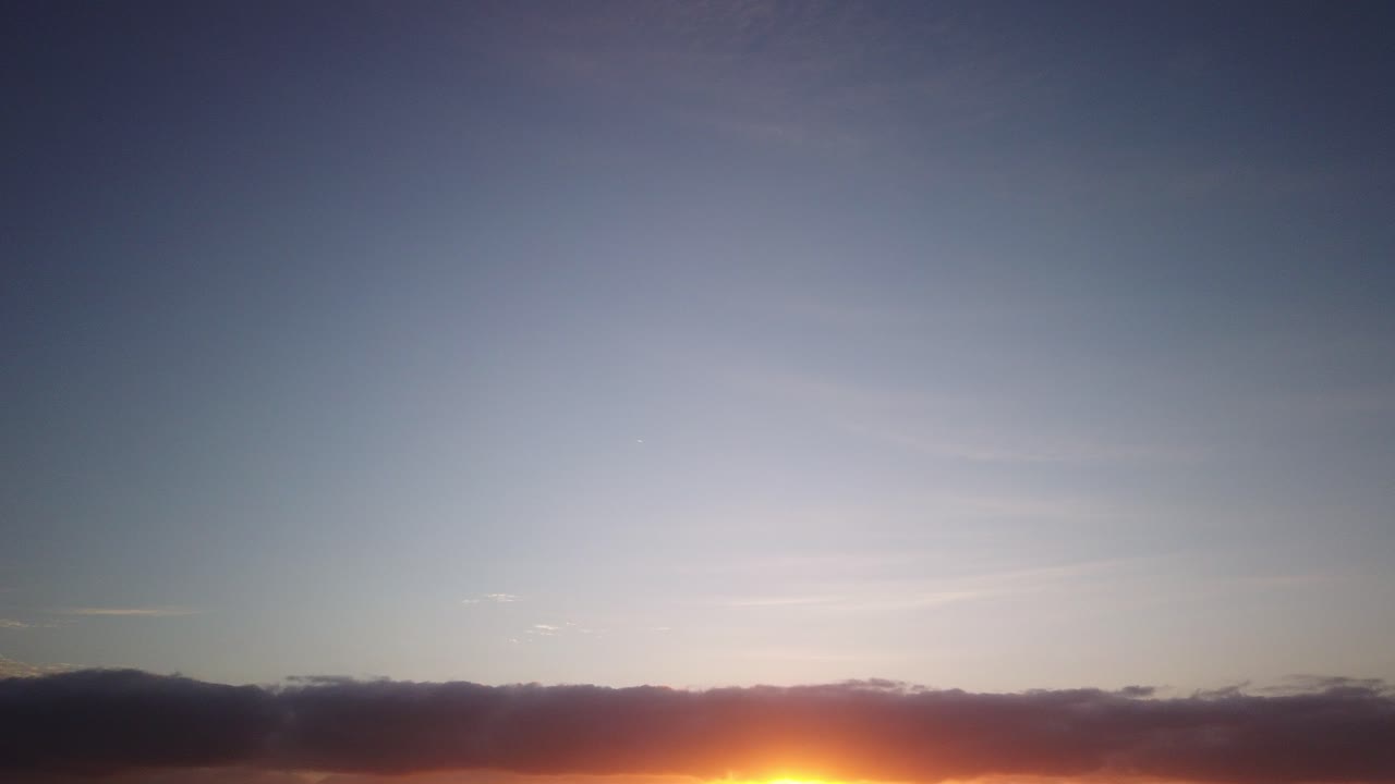Golden sunrise hyperlapse, over an ocean beach as high and low clouds, rush past each other