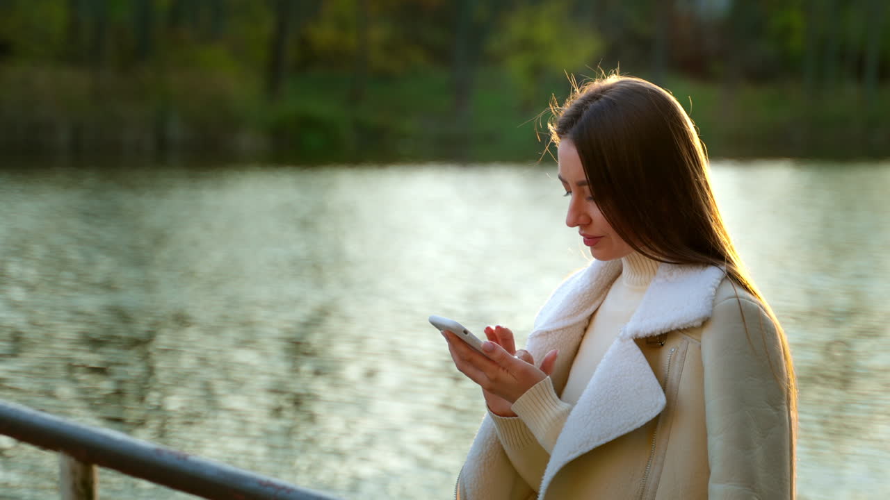 Woman using a phone by a lake in autumn