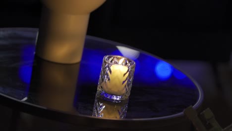 candle in glass container lit on glass table in party decoration