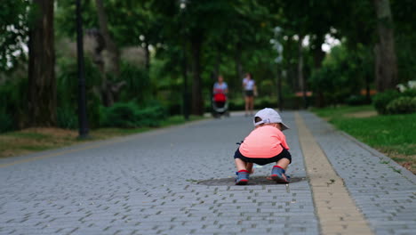 rear view of a little toddler touching the paved ground in the park. baby boy trying to walk on his hands.