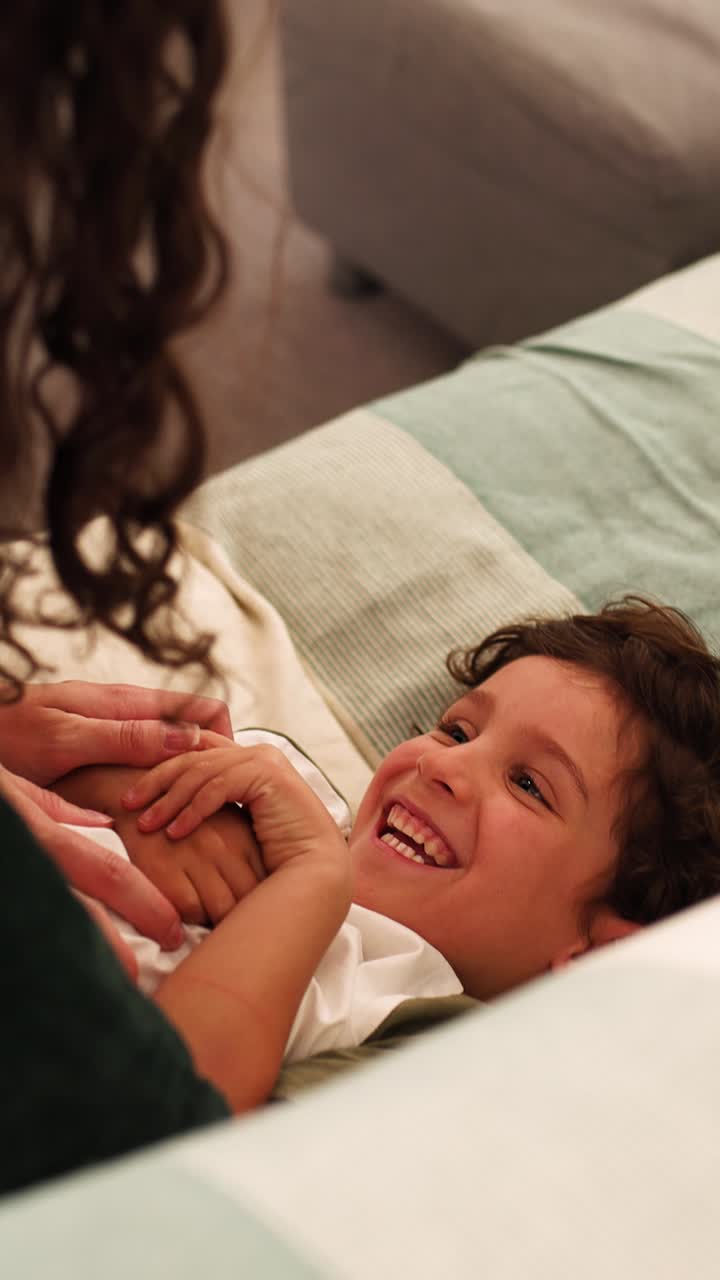 Happy child lying on bed, holding mother's hands and smiling